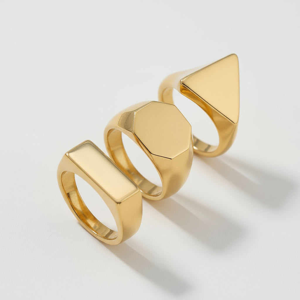 Three gold rings with geometric designs on a beige background