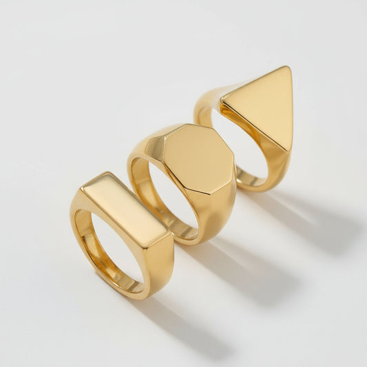 Three gold rings with geometric designs on a beige background